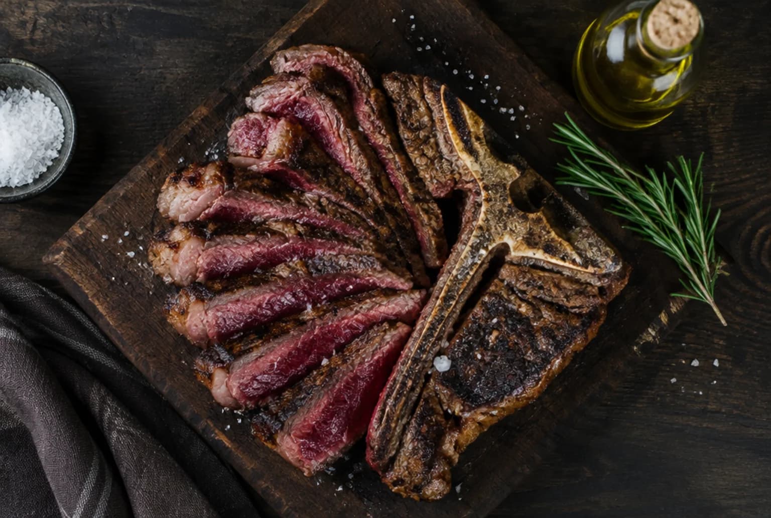 Aufgeschnittenes Bistecca alla Fiorentina auf dunklem Holzbrett, rosa Kern und Meersalz